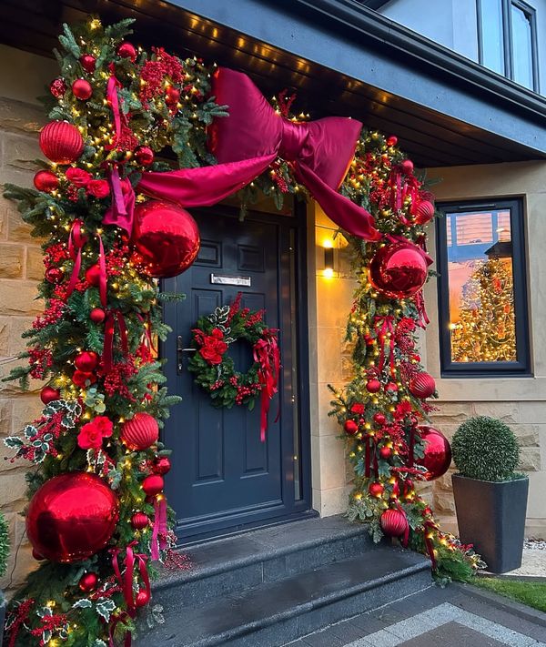 A front entrance framed in garland with red ornaments and an oversized bow
