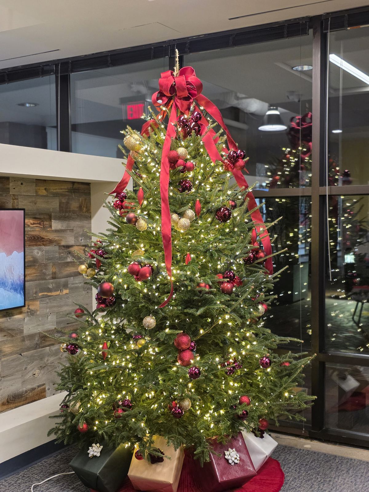 A Curator Atelier tree with red ribbon and wrapped gifts beneath in a client office, December 2025