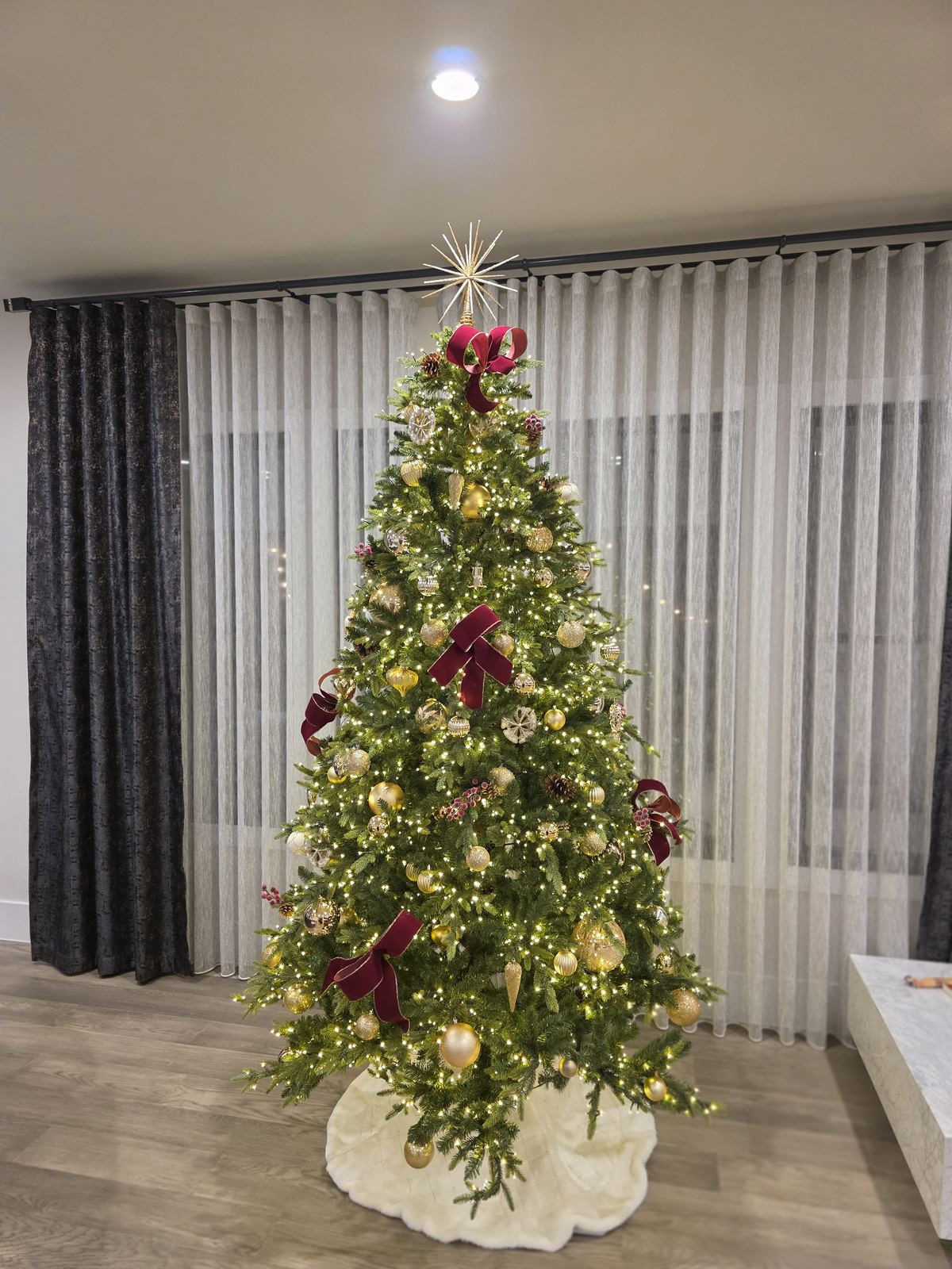 A Curator Atelier tree with burgundy ribbon and a white skirt in a client residence, December 2025